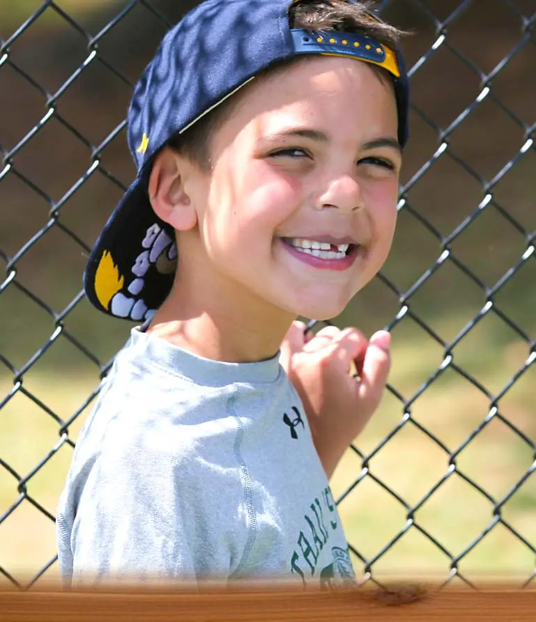 young camper smiling with fence behind him
