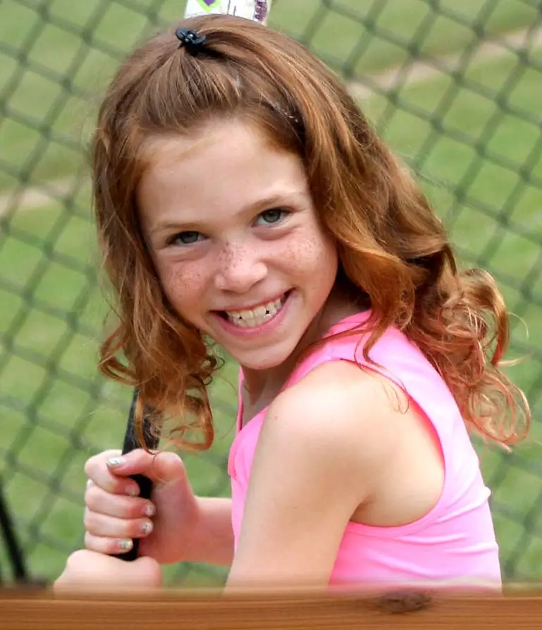 girl camper smiling and swinging a bat